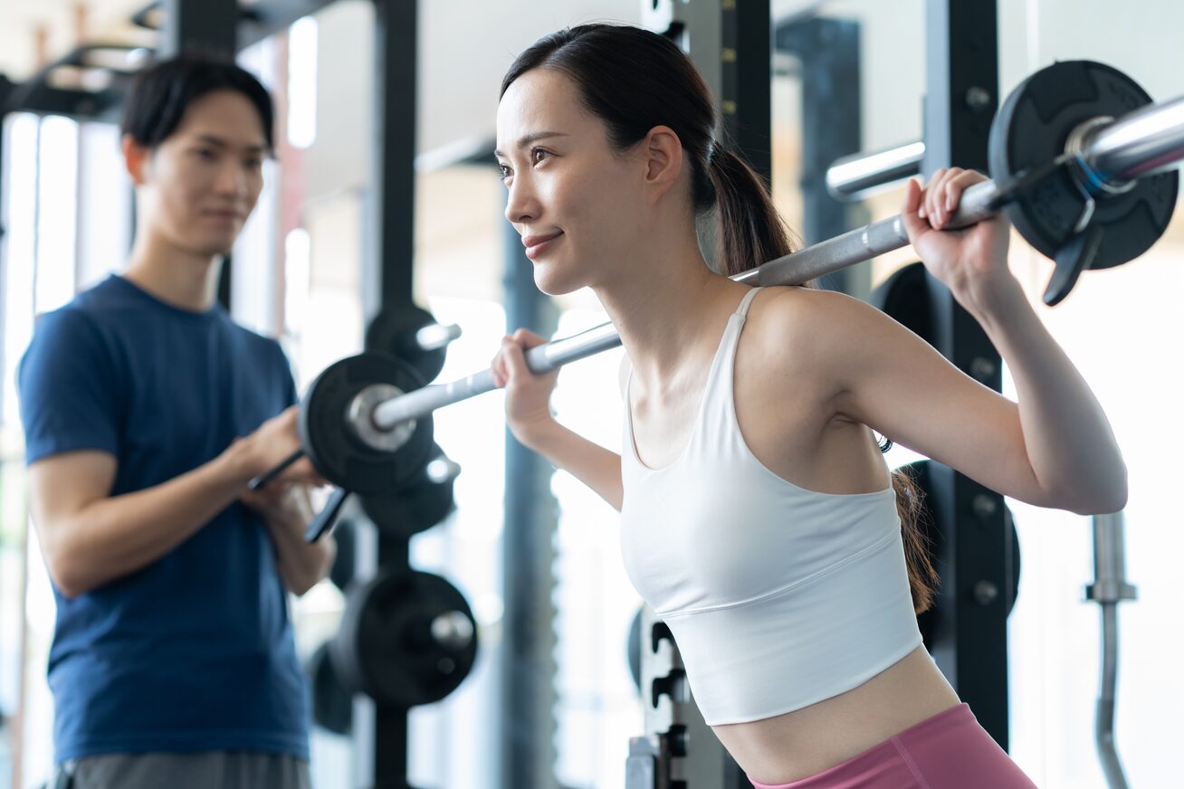 トレーナーの補助を受けながらバーベルスクワットに取り組む女性