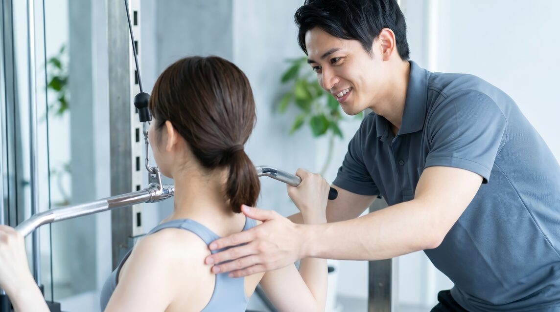 トレーナーがマシンを使う女性の姿勢を指導している様子