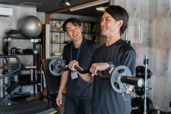 トレーナーがバーベルの使い方を指導している様子