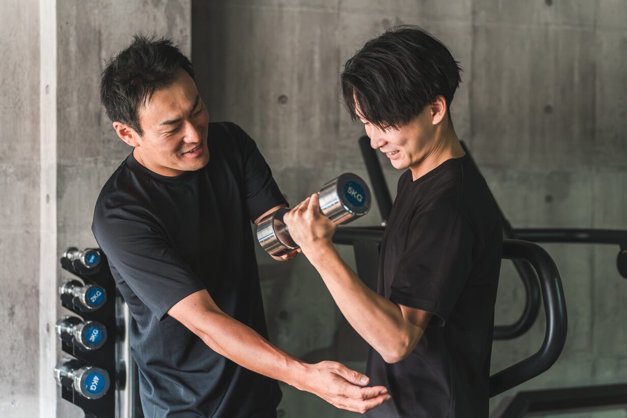 トレーナーの指導を受けながらダンベルを持ち上げる男性