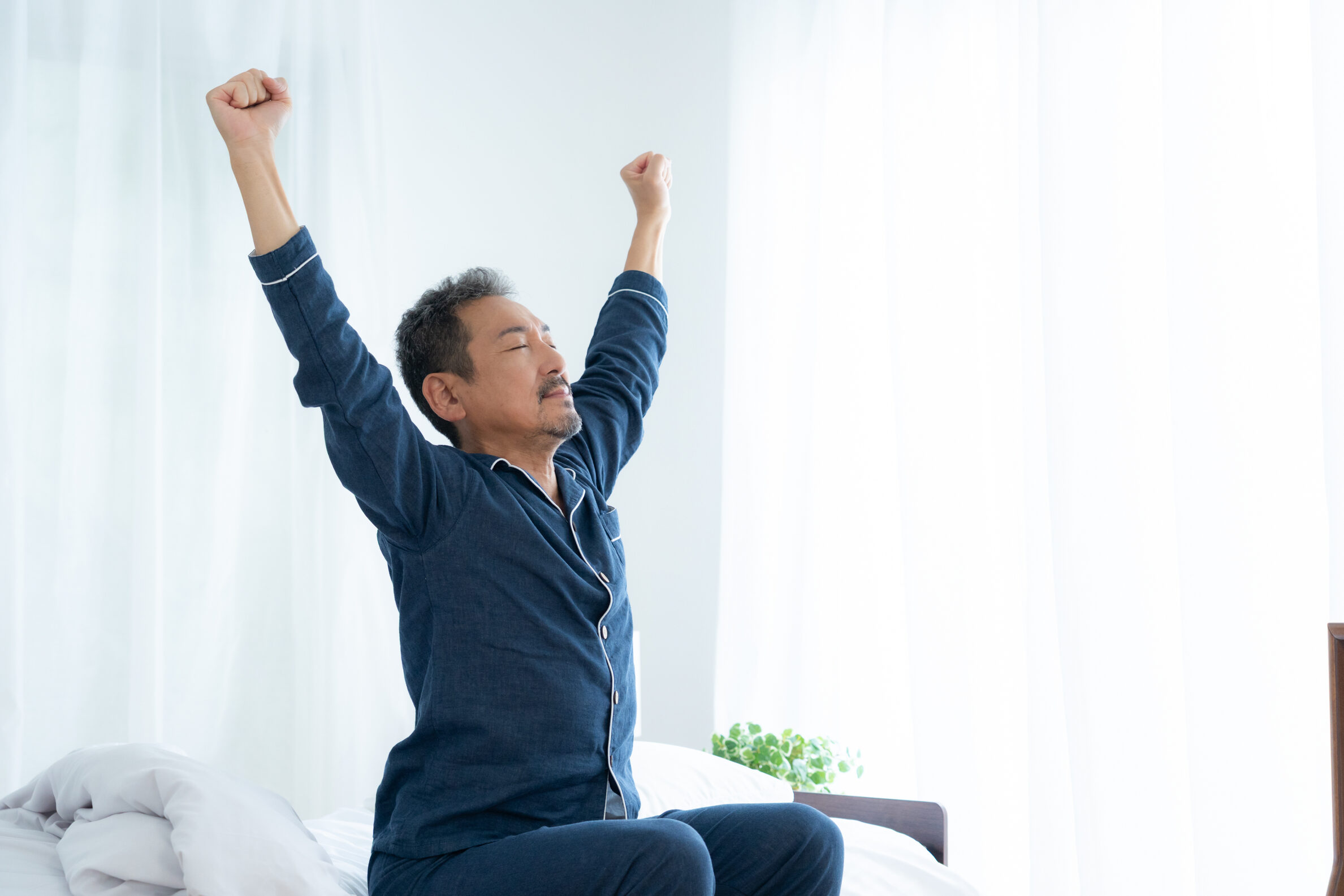 ベッドの上で両手を上げて伸びをする男性